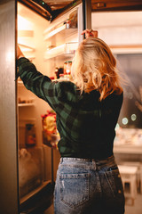 Woman taking food out of open fridge at home