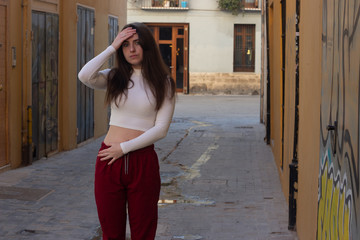 Portrait of worried attractive young woman keeps hand on forhead, in the city, white top and red pants, dark air. Place for your text in copy space.
