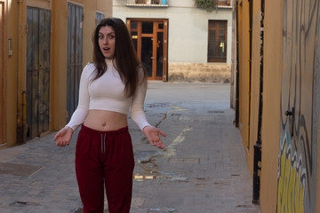 Portrait of caucasian young woman with stunned expression, keeps mouth opened, in the city, white top and red pants. Place for your text in copy space.