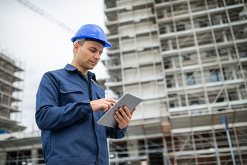 Worker using his tablet in front of a construction site