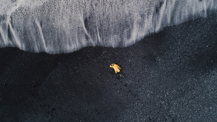 A young traveler in yellow clothes lies on the black sand beach in Iceland