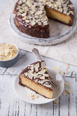 Piece Slice of Сheesecake with Chocolate, Caramel, Peanut Paste, Nougat Layered Cake on white table background