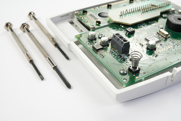 Home alarm control panel repairing. Open Electronic board panel with screwdrivers on a white...