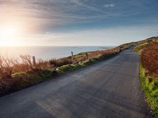 Fototapeta premium Road by ocean at sunset time. Calm blue sky. Nobody, West coast of Ireland.