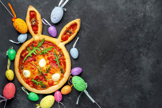 Festive Easter pizza in the form of a rabbit with eggs, multi-colored  Easter eggs on a stone background with copy space for your text.