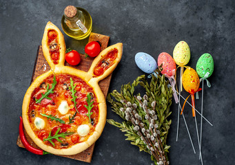 Festive Easter pizza in the form of a rabbit with eggs, colorful  Easter eggs and willow on a stone background. Easter celebration concept.