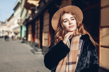 Female fashion. Stylish woman wearing fur coat, beige hat and scarf. Spring accessories. Portrait of young girl outdoors