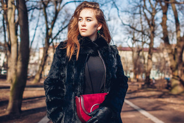 Female fashion. Stylish woman wearing fur coat and holding red purse. Spring clothes accessories. Outdoors portrait
