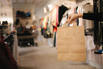 Hand with craft bag in clothing store. Female hand hilding bag with purchase