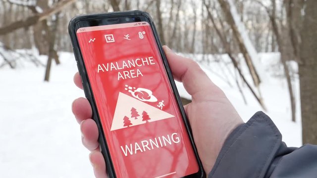 Receiving an avalanche warning message on the mobile phone while hiking in a forest during winter.