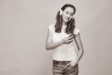 A brunette girl in summer clothes listens to music in headphones and looks into a smartphone.