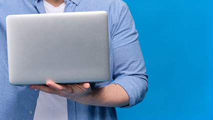 A man in a blue shirt is holding a laptop. Copy space.