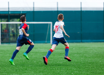 Boys in white and blue sportswear plays  football on field, dribbles ball. Young soccer players with ball on green grass. Training, football, active lifestyle for kids concept 