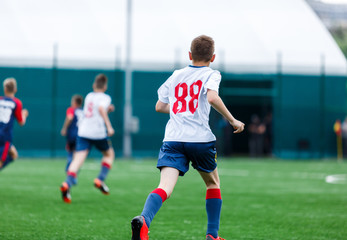 Obraz premium Chłopcy w biało-niebieskich strojach sportowych grają w piłkę nożną na boisku, dryblują piłkę. Młodzi piłkarze z piłką na zielonej trawie. Trening, piłka nożna, aktywny tryb życia dla koncepcji dzieci