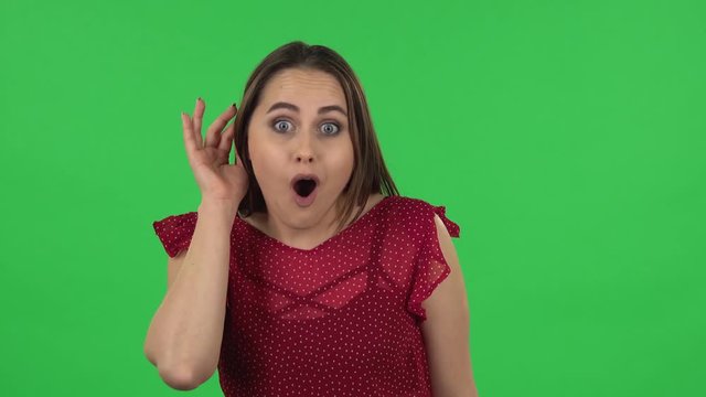 Portrait of tender girl is holding hand near ear trying to listen to news expressing communication concept. Green screen