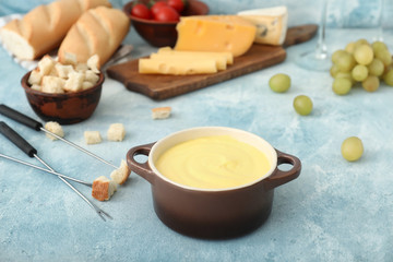 Cheese fondue with snacks on color background