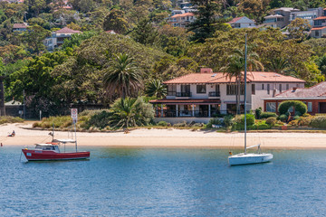 Sydney, Australia - December 11, 2009: Upscale house with red roof on sandy beach with green vegetation on northern shore  of bay behind blue bay water.