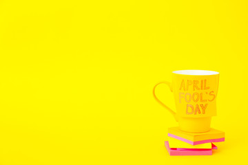 Papers with cup on color background. April Fool's Day prank