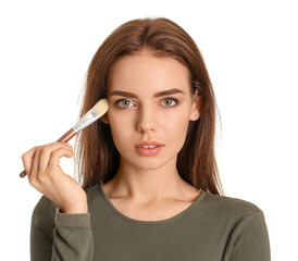 Beautiful young woman applying makeup on white background