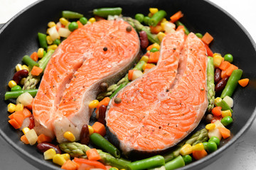 Frying pan with raw salmon steaks and vegetables on table, closeup