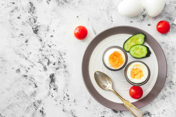 Plate with tasty boiled eggs and vegetables on light background