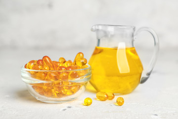 Bowl with pills and jug of oil on white background