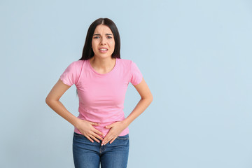 Young woman suffering from menstrual cramps on color background