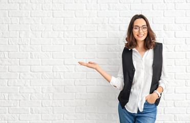 Portrait of beautiful young businesswoman showing something on white brick background