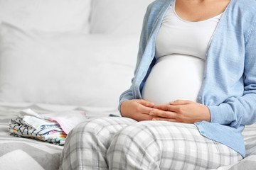 Pregnant woman with baby clothes in bedroom, closeup