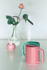 Pink rose flower and twin half tea mugs in salmon pink and fresh mint green. Minimalist design for your house in pastel colors. Modern interior decor, romantic gifts. Greeting card for Valentine day.