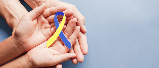 Adult and child hands holding blue and yellow ribbon shaped paper, Down syndrome awareness , World...