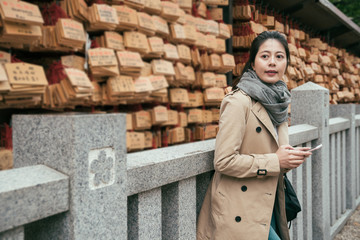 Beautiful small wooden wishing plaques at tenmangu shrine osaka. young girl traveler in autumn time travel in japan. woman tourist leaning on stone wall using cellphone texting message online.