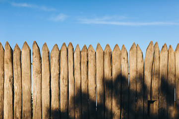 Fence from a stockade fence against the blue sky. Pointed logs, old wood texture. Copy space.