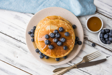 Close up of fluffy pancakes with maple syrup and blueberries against white wooden background