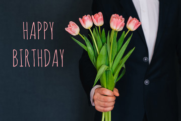 Man giving a bouquet of pink flowers tulips. Greeting card with text Happy birthday
