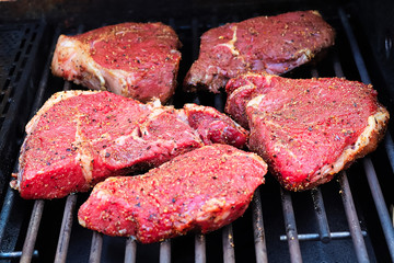 Raw seasoned steaks on a BBQ grill
