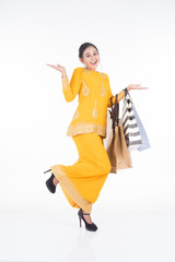 A beautiful Asian female model in a traditional dress modern kurung carrying shopping bags isolated on white background. Eidul fitri festive preparation shopping concept. Full length portrait.
