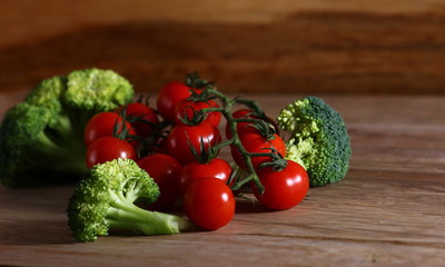 fresh cherry tomatoes on a branch and broccoli on a wooden surface