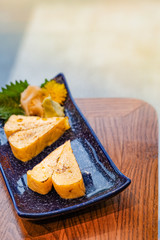 Japanese food, Tamago or grilled rolled omelet in a small blue plate and shape-like a Heart on wooden table