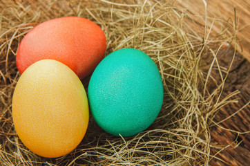 Fototapeta na wymiar Nest with colorful easter eggs on the dark wooden background, close-up, top view, selective focus.