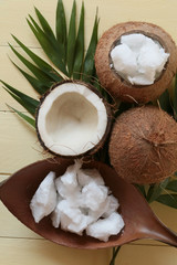 Fototapeta na wymiar Coconut oil. Large pieces of coconut oil in a coconut shell, coconut nuts on yellow wooden board background. Organic Bio Coconut Oil