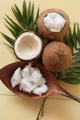 Coconut oil. Large pieces of coconut oil in a coconut shell, coconut nuts and palm branch on yellow wooden  background. Organic Bio Coconut Oil