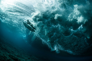 Underwater view of the woman surfer passing the powerfull ocean wave