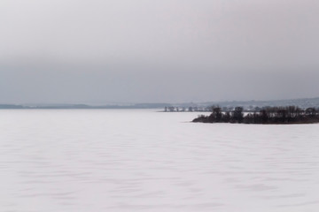Obraz premium Landscape view of a large frozen river on a gray cloudy day.