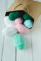 scatter oval acrylic colorful wool yarn thread skeins lying with kraft paper brown package on white...