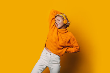 Fototapeta premium A gorgeous girl listening to music and being completely isolated from our world in her yellow headphones and charming music on background