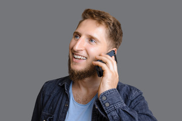 A young caucasian entrepreneur with beard looks happily while being called by somebody standing on a grey background