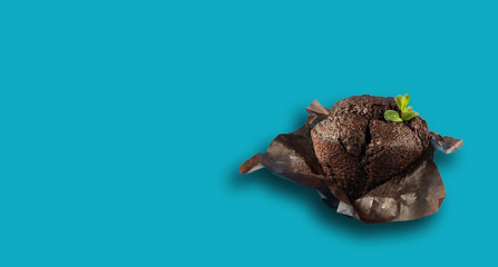 Muffin with chocolate decorated with a leaf of mint isolated on a blue background. close-up, copy space