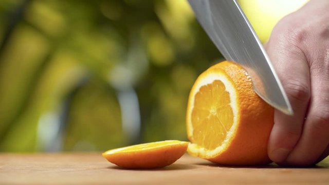 Close up male hand slicing an orange on green natural background. Juice flows over a knife. Juicy fruits. Healthy lifestyle and eating concept