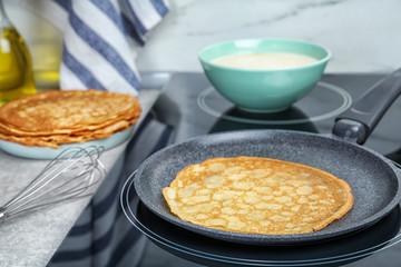Delicious thin pancake in frying pan on induction stove, closeup